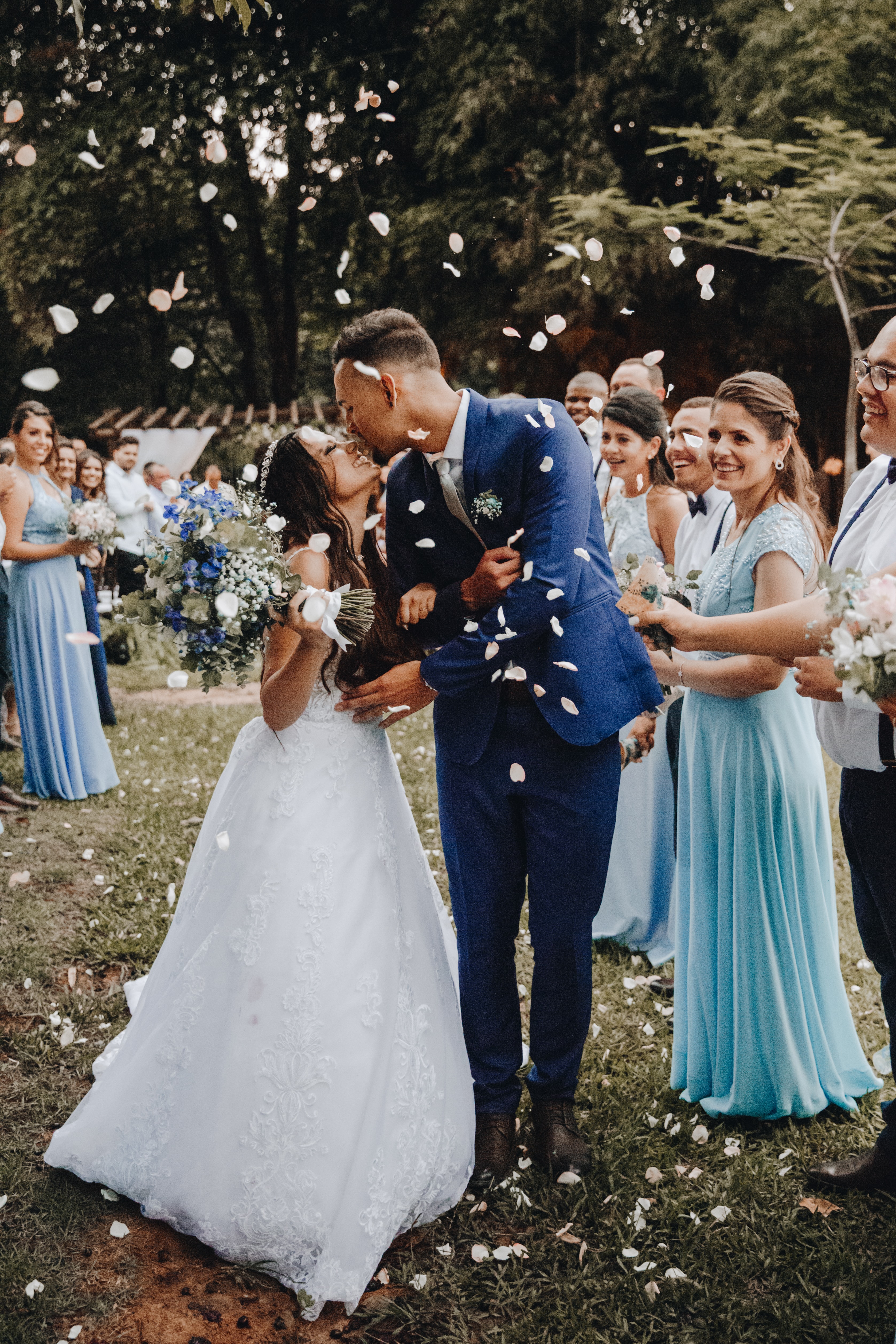 wedding couple embracing with guests behind them; flower petals in the air